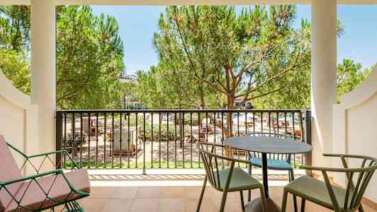 Parveke, jossa pöytä, tuoleja ja näkymä vehreisiin puihin. (Tekoälyn luoma teksti)