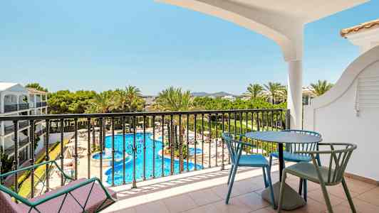 Näköala parvekkeelta, jossa on pöytä ja tuolit, kohti uima-allasta ja ympäröivää vehreyttä. (Tekoälyn luoma teksti)