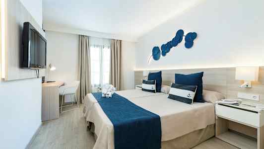 Hotellihuone, jossa kaksi sänkyä ja merellinen teema, siniset vuodevaatteet ja koristeelliset tyynyt. (Tekoälyn luoma teksti)