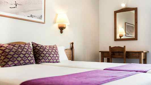 Hotellihuone, jossa on kaksi violetilla vuodevaatteella peitettyä erillistä sänkyä, peili ja kirjoituspöytä. (Tekoälyn luoma teksti)