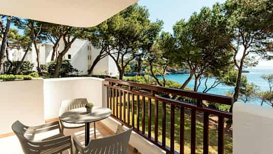 Parveke, jossa pöytä ja tuolit, näkymä puihin ja mereen. (Tekoälyn luoma teksti)