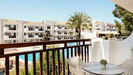 Näkymä parvekkeelta, jossa pöytä ja tuolit, valkoiseen rakennukseen ja uima-allasalueelle. (Tekoälyn luoma teksti)