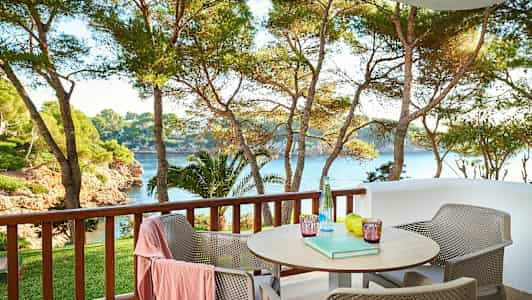 Ulkoterassi, jossa pöytä ja tuoleja, näkymä puihin ja mereen. (Tekoälyn luoma teksti)
