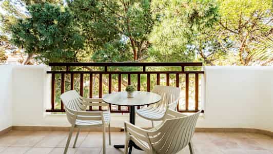 Parveke, jossa on neljä tuolia ja pöytä kaiteen sekä vihreiden puiden edessä. (Tekoälyn luoma teksti)