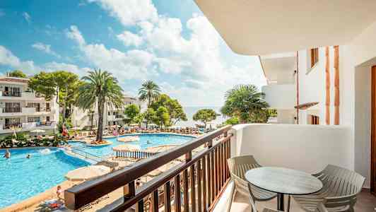 Näkymä parvekkeelta uima-altaalle, jota ympäröivät aurinkotuolit, palmupuut ja rakennukset. (Tekoälyn luoma teksti)