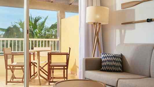 Sisustus, jossa sohva ja tyyny etualalla sekä näkymä kalustetulle parvekkeelle. (Tekoälyn luoma teksti)