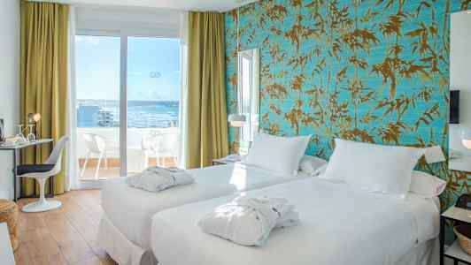 Hotellihuone, jossa on kaksi valkoista sänkyä ja parvekkeen ovi, joka johtaa terassille merinäköalalla. (Tekoälyn luoma teksti)