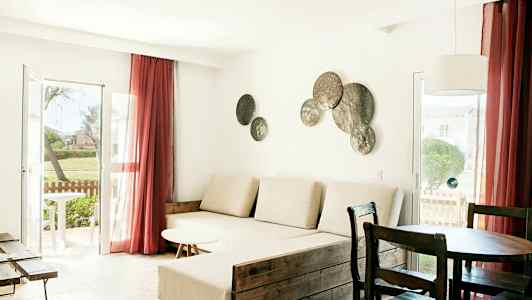 Olohuone, jossa on vaaleat huonekalut, suuri ikkuna punaisilla verhoilla ja koristeita seinällä. (Tekoälyn luoma teksti)