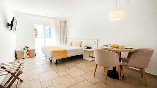 Hotellihuone, jossa on sänky, ruokapöytä tuoleineen ja televisio seinällä. (Tekoälyn luoma teksti)