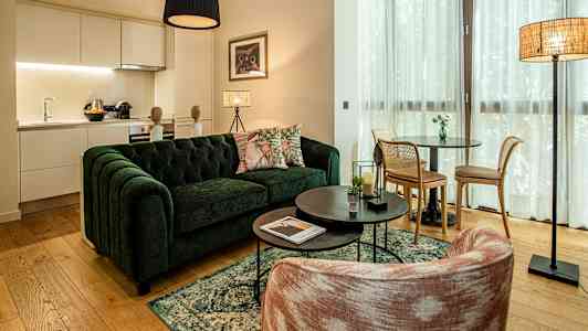 Olohuone, jossa on vihreä sohva, sohvapöytä ja ruokailutila. Keittiö näkyy taustalla. (Tekoälyn luoma teksti)