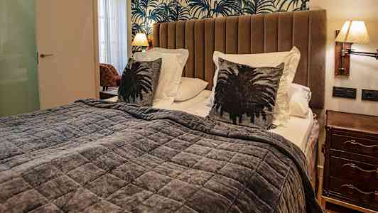 Makuuhuoneessa on sänky, jossa on ruskeat tyynyt, harmaa päiväpeitto ja kuvioitu seinätausta. (Tekoälyn luoma teksti)