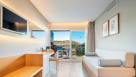 Moderni hotellihuone, jossa puusisustus, sohva ja näkymä merelle lasioven läpi. (Tekoälyn luoma teksti)