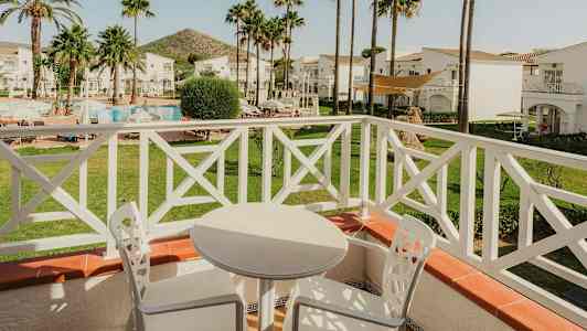 Näkymä parvekkeelta, jossa valkoisia ulkokalusteita, puutarhaan, jossa on uima-allas ja palmuja. (Tekoälyn luoma teksti)