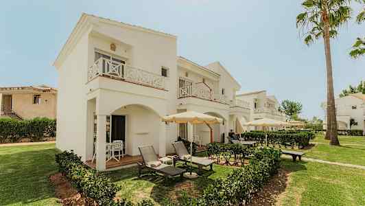 Hotellin valkoiset kaksikerroksiset rakennukset parvekkeineen ja terasseineen, joita ympäröi vehreys. (Tekoälyn luoma teksti)