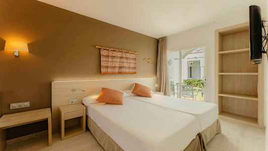 Hotellihuone, jossa on kaksi yhden hengen vuodetta, koristeelliset tyynyt ja taidetta seinällä. Ikkunasta näkymä puutarhaan. (Tekoälyn luoma teksti)