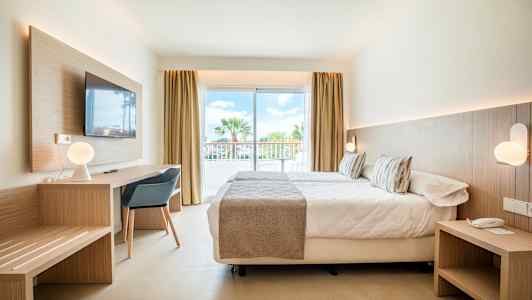 Modernisti sisustettu hotellihuone, jossa on sänky, kirjoituspöytä ja suuret lasiovet parvekkeelle. (Tekoälyn luoma teksti)