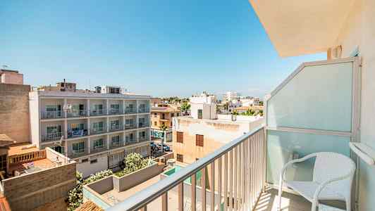 Näkymä parvekkeelta, joka näyttää asuinalueen rakennuksineen ja puineen kirkkaan sinisen taivaan alla. (Tekoälyn luoma teksti)