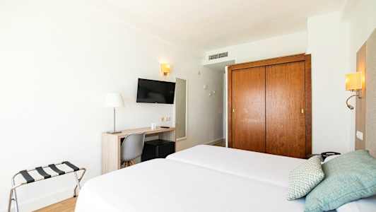 Hotellihuone, jossa kaksi erillistä vuodetta, kirjoituspöytä, tuoli, televisio ja vaatekaappi. (Tekoälyn luoma teksti)