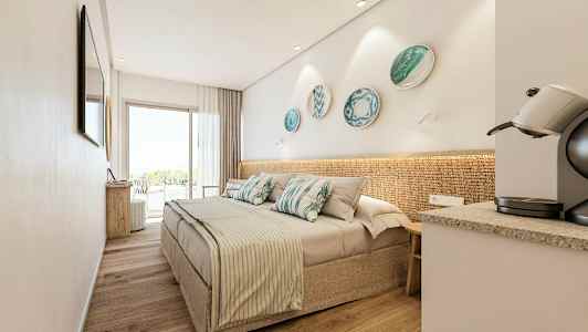 Moderni hotellihuone, jossa on parivuode, koristeelliset koristekulhot seinällä, kahvikone ja suuret lasiovet, jotka johtavat parvekkeelle. (Tekoälyn luoma teksti)