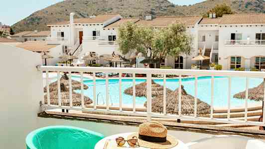 Näkymä parvekkeelta uima-altaalle ja rakennuksille, taustalla vuoria. (Tekoälyn luoma teksti)