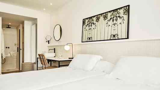 Valoisa hotellihuone, jossa sänky, kirjoituspöytä ja kylpyhuone. (Tekoälyn luoma teksti)