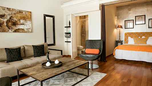 Hotellihuone, jossa istuinryhmä, pöytä ja sänky oransseilla yksityiskohdilla. (Tekoälyn luoma teksti)