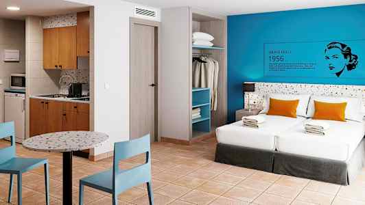 Hotellihuone, jossa on kaksi sänkyä, keittiö, ruokapöytä ja avoin vaatekaappi. (Tekoälyn luoma teksti)