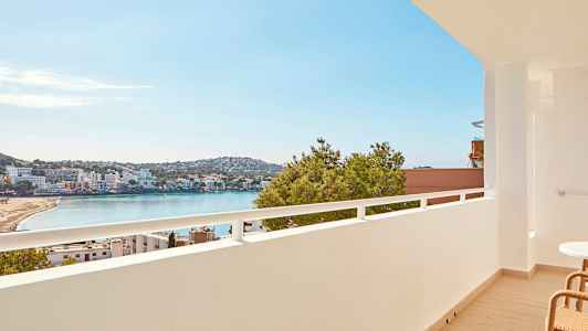 Näkymä parvekkeelta rannalle lahden äärellä, taustalla rakennuksia ja vihreitä alueita. (Tekoälyn luoma teksti)