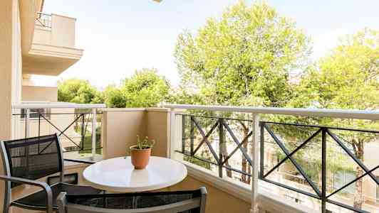 Parveke, jossa pöytä ja tuolit, näkymä puihin ja rakennuksiin. (Tekoälyn luoma teksti)