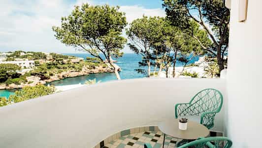 Parveke, jossa on kaksi tuolia ja pöytä, näkymä merelle ja mäntymetsään. (Tekoälyn luoma teksti)