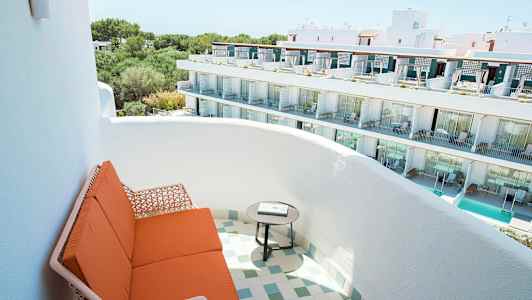 Kuvassa on parveke, jossa on oransseja istuimia ja pyöreä pöytä, näkymä valkoiseen rakennukseen, jossa on useita kerroksia ja parvekkeita. (Tekoälyn luoma teksti)