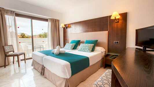 Hotellihuone, jossa on kaksi erillistä vuodetta, televisio ja parveke taustalla. (Tekoälyn luoma teksti)