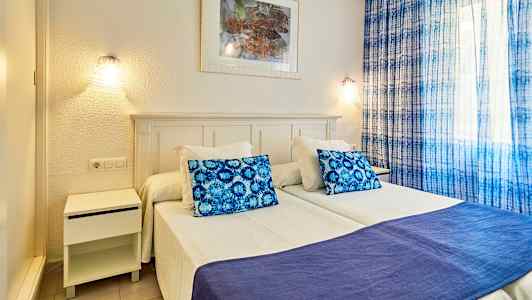 Kuva makuuhuoneesta, jossa kaksi erillistä sänkyä, sininen tyyny ja peitto sekä siniset verhot. (Tekoälyn luoma teksti)