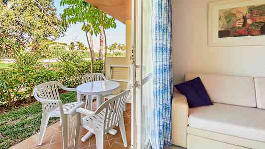 Terassi, jossa muovikalusteita ja puutarha sekä sisäosa, jossa sohva ja taide seinällä. (Tekoälyn luoma teksti)