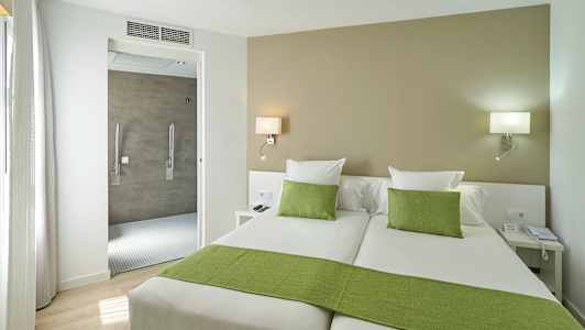 Hotellihuone jossa kaksi erillistä sänkyä, vihreät vuodevaatteet ja aukko kylpyhuoneeseen. (Tekoälyn luoma teksti)