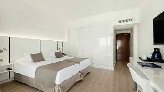 Hotellihuone, jossa on kaksi yhden hengen sänkyä, kirjoituspöytä ja televisio. (Tekoälyn luoma teksti)