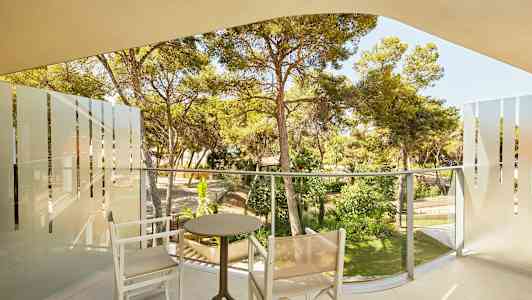 Parveke, jossa on kaksi tuolia ja pöytä, näkymä vehreään puutarhaan. (Tekoälyn luoma teksti)