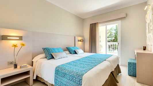 Hotellihuone, jossa on parivuode, sininen koristetyyny ja sininen päiväpeitto. (Tekoälyn luoma teksti)