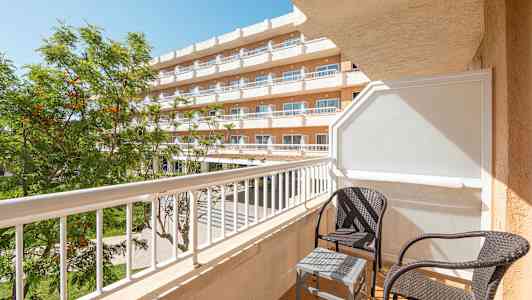 Parveke, jossa kaksi rottinkituolia ja pieni pöytä hotellin yhteydessä. (Tekoälyn luoma teksti)