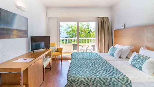 Hotellihuone, jossa kaksi sänkyä, työpöytä ja ikkuna näkymällä parvekkeelle. (Tekoälyn luoma teksti)