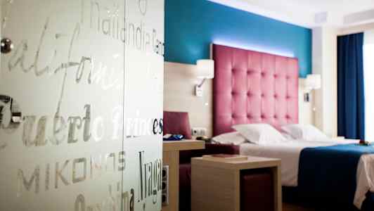 Hotellihuone värikkäällä sisustuksella, sänky ja pöytä. (Tekoälyn luoma teksti)