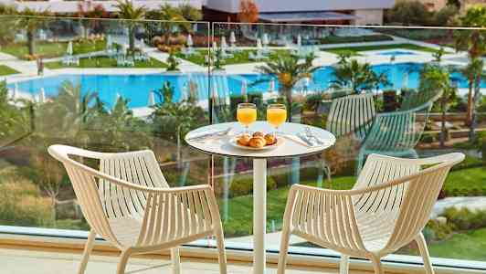 Kaksi tuolia pöydän ääressä, jolla on aamiainen, huoneessa uima-allasalueelle avautuvalla näköalalla. (Tekoälyn luoma teksti)