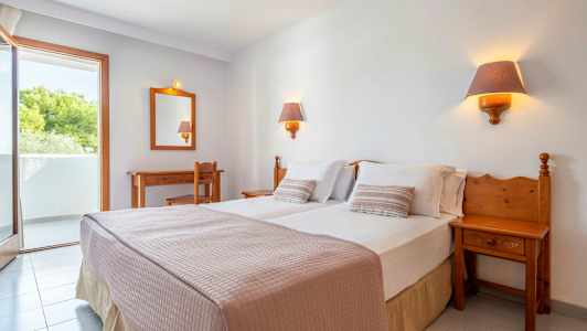 Hotellihuone, jossa on parivuode, kaksi yöpöytälamppua, työpöytä, tuoli ja parveke. (Tekoälyn luoma teksti)