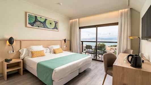Kuva hotellihuoneesta, jossa on parivuode, työpöytä ja näkymä merelle. (Tekoälyn luoma teksti)