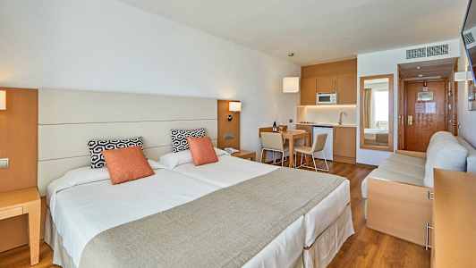 Studio, jossa on kaksi vuodetta, istuimet ja keittiö. (Tekoälyn luoma teksti)