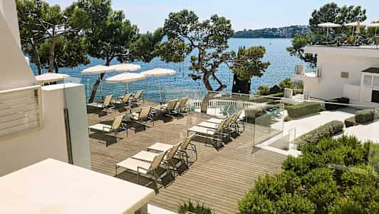 Aurinkoterassi, jossa aurinkotuoleja ja varjoja meren rannalla. (Tekoälyn luoma teksti)