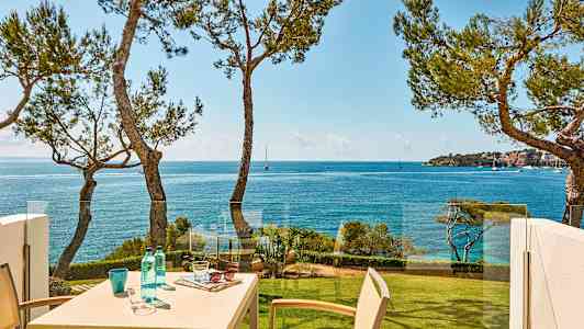 Näkymä merelle, jossa parvekkeella sijaitseva pöytä, ympäröitynä puilla. (Tekoälyn luoma teksti)