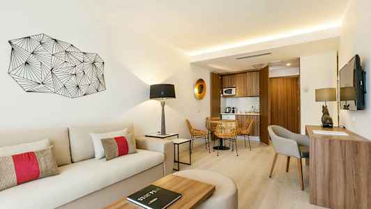 Valoisa ja moderni hotellihuone, jossa istumapaikka, kirjoituspöytä, sohva ja pieni keittiö. (Tekoälyn luoma teksti)