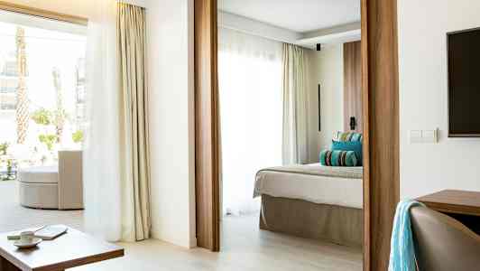 Moderni hotellihuone, jossa vaalea sisustus, runsaasti luonnonvaloa ja mukava sänky. (Tekoälyn luoma teksti)