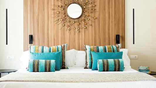 Kuva sängystä, jonka päällä on värikkäitä tyynyjä ja koristeellinen peili seinällä. (Tekoälyn luoma teksti)